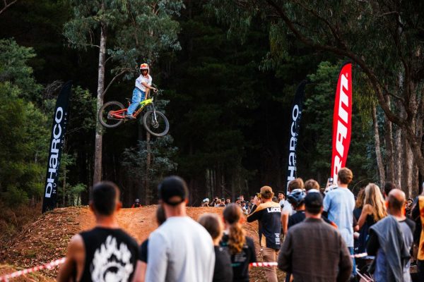 mountain bike rider jumping dirt jumps in full face surrounded by sponsor flags at mystic bike park