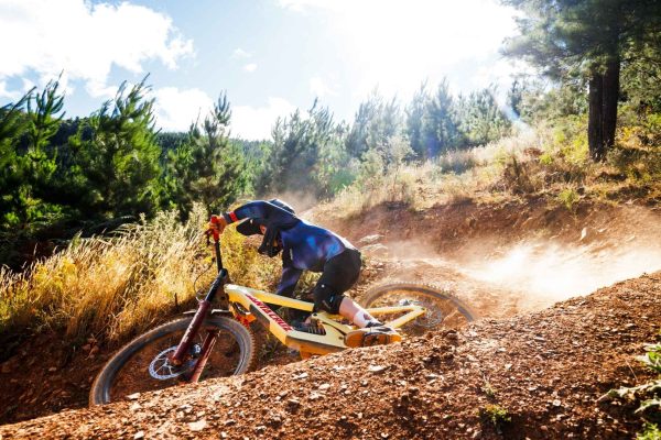 Summer Sesh at Mystic Bike Park Bright Off Road mountain bike and rider turning fast corner with pine tree and mountains in backdrop at Mystic bike park