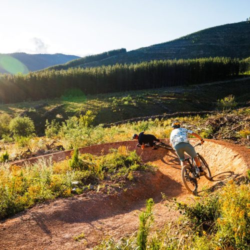 two mtb riders on off road trail in amongst mountain scape backdrop at mystic in bright